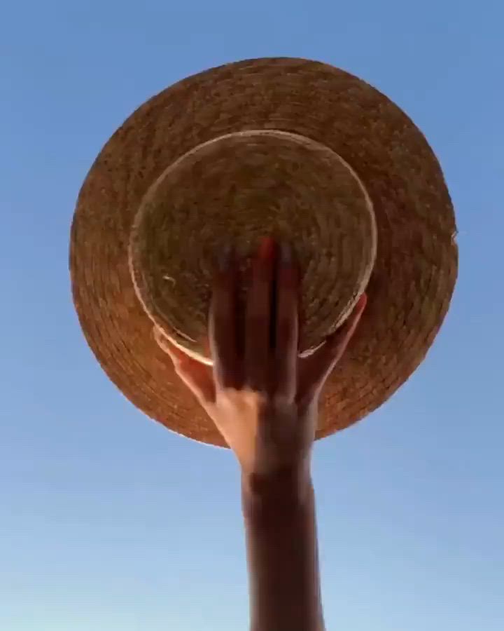 This may contain: a person's hand reaching up into the sky with a straw hat on their head