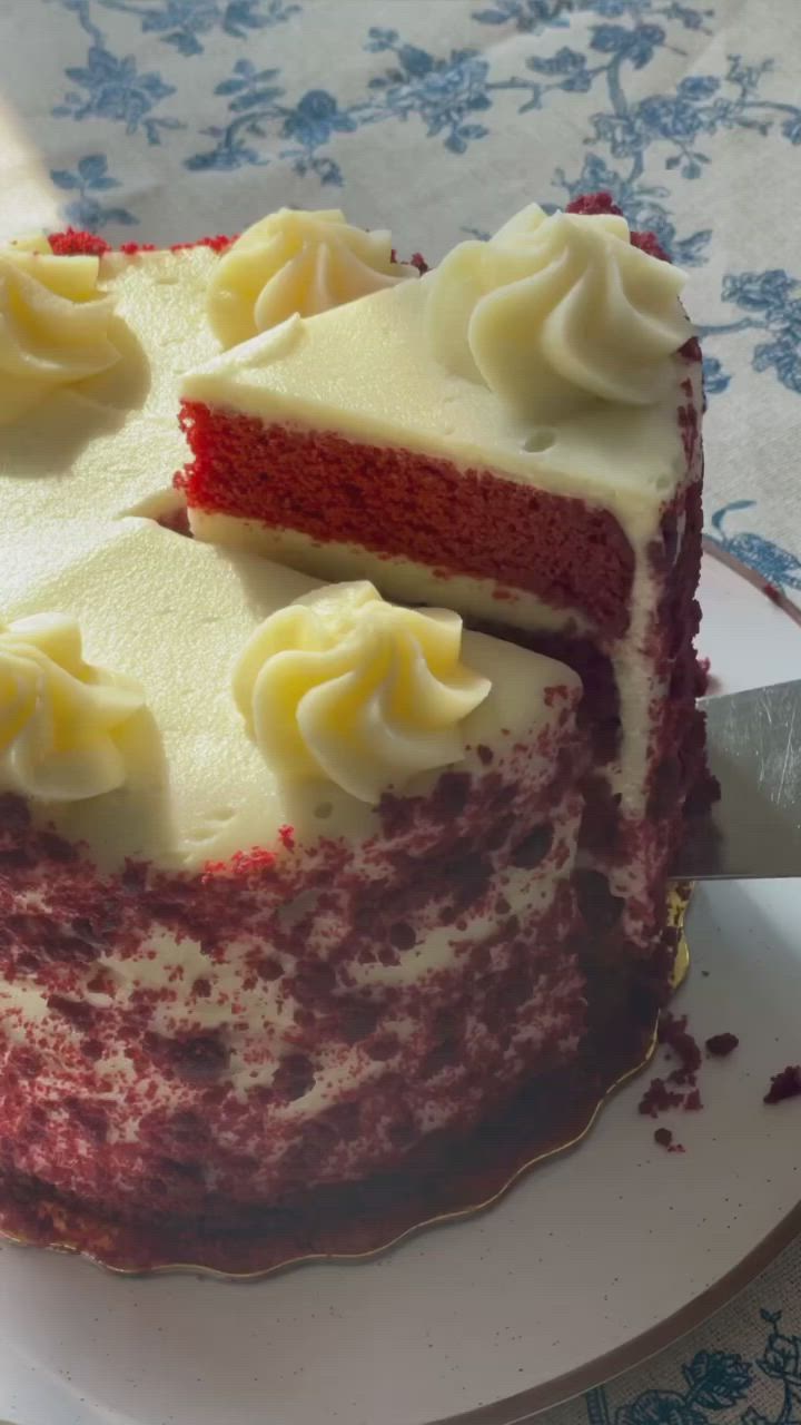 This may contain: a slice of red velvet cake with white frosting on a blue and white plate