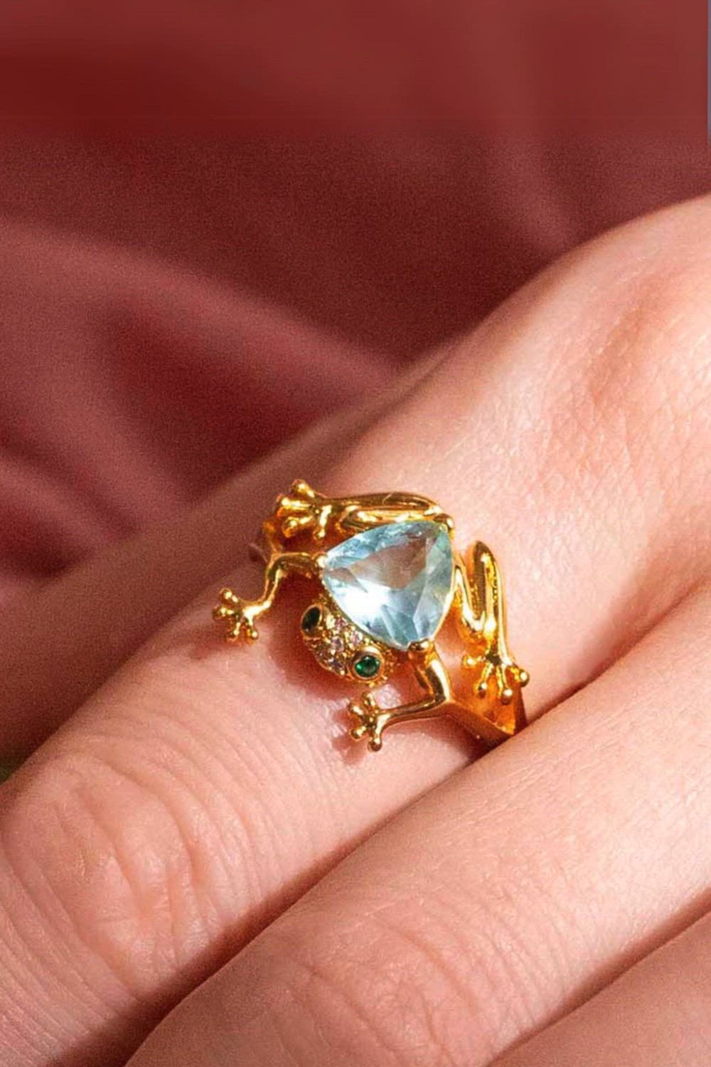 This contains: a woman's hand with a gold ring with a blue topazte and