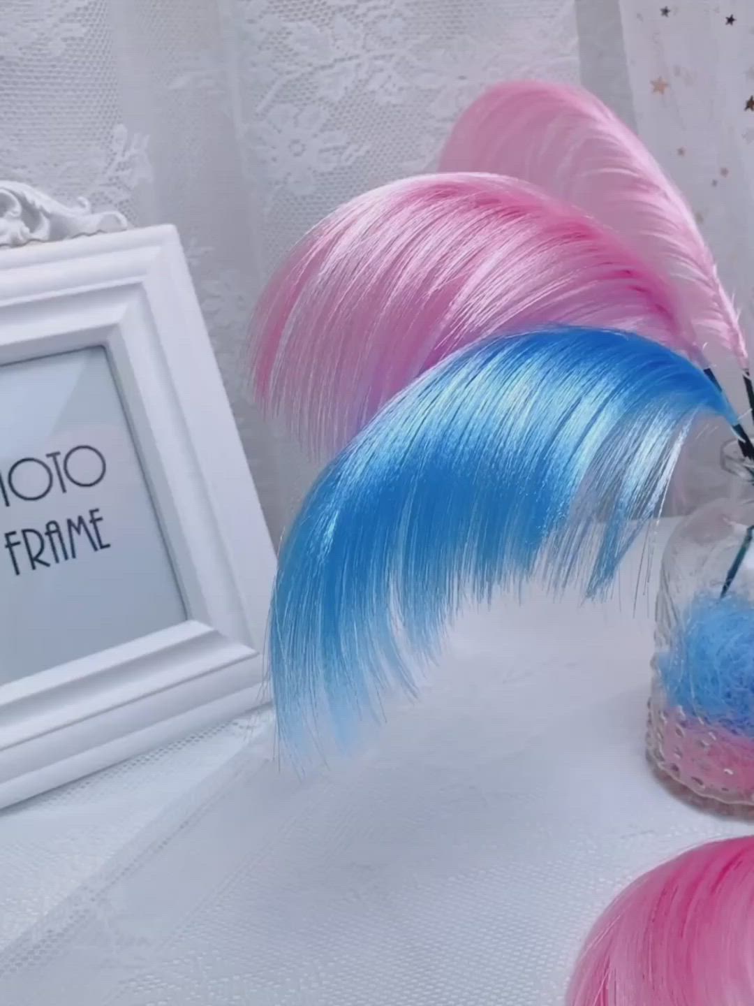 This may contain: pink and blue feathers in a vase next to a photo frame on a white tablecloth