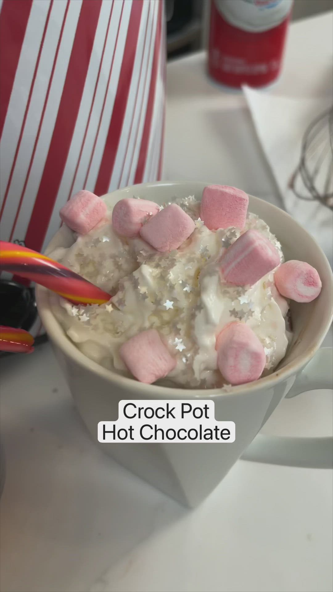 This may contain: a woman holding a cup filled with marshmallows and hot chocolate in a crock pot