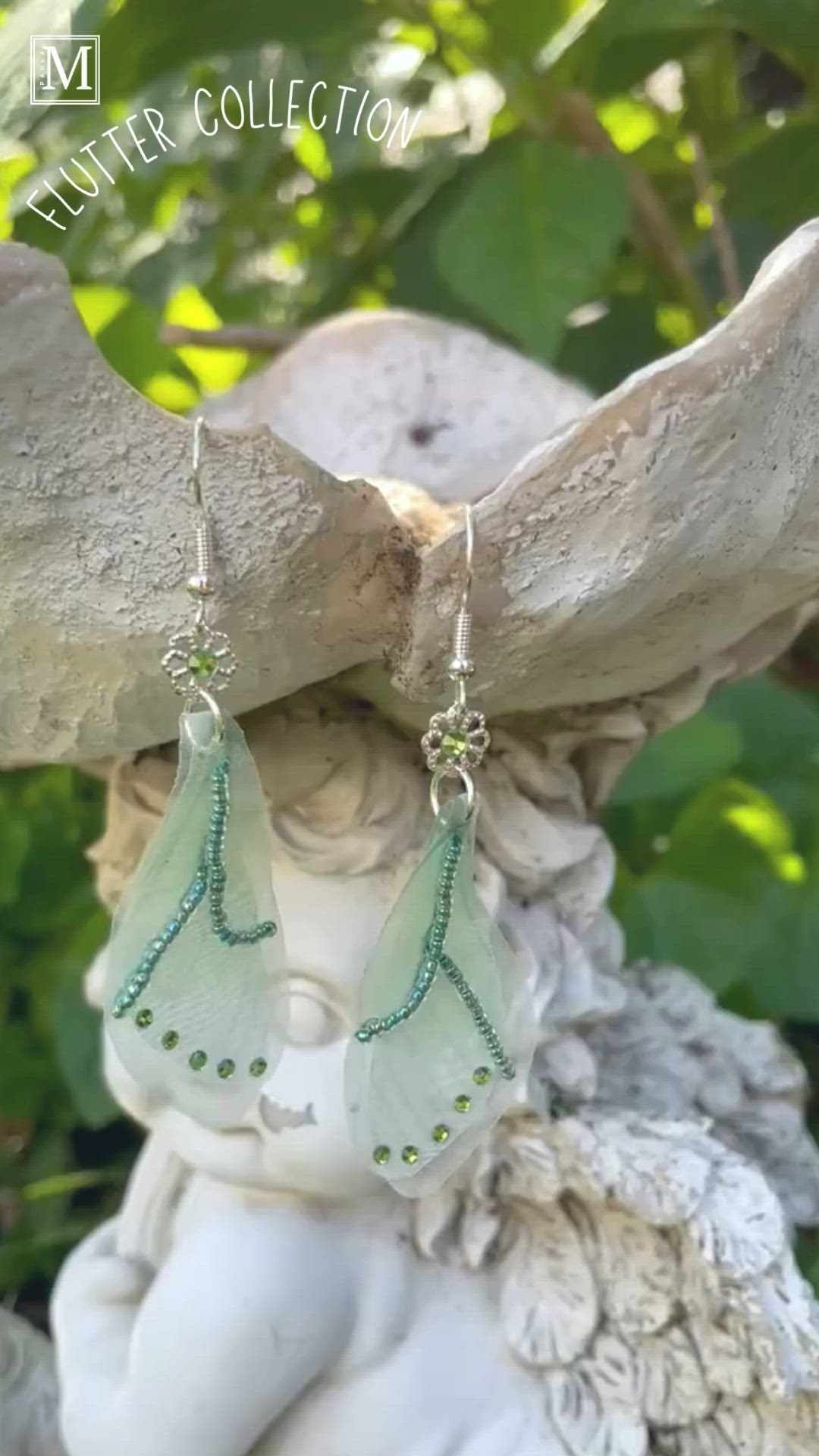 This contains: Sheer green fabric butterfly wing earrings with green crystals along the bottom edge and beading. a flower bead with a green crystal connects the wing to the french ear wires.