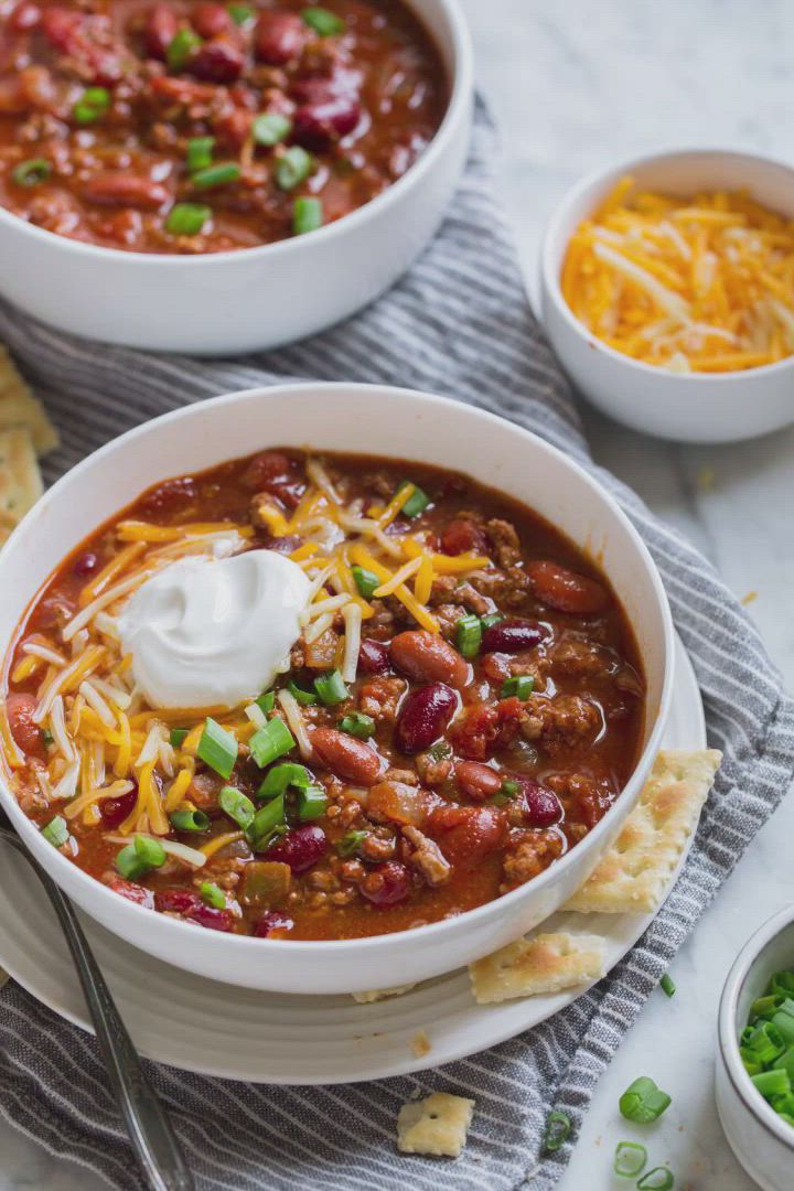 This may contain: two bowls of chili with sour cream and tortilla crackers on the side