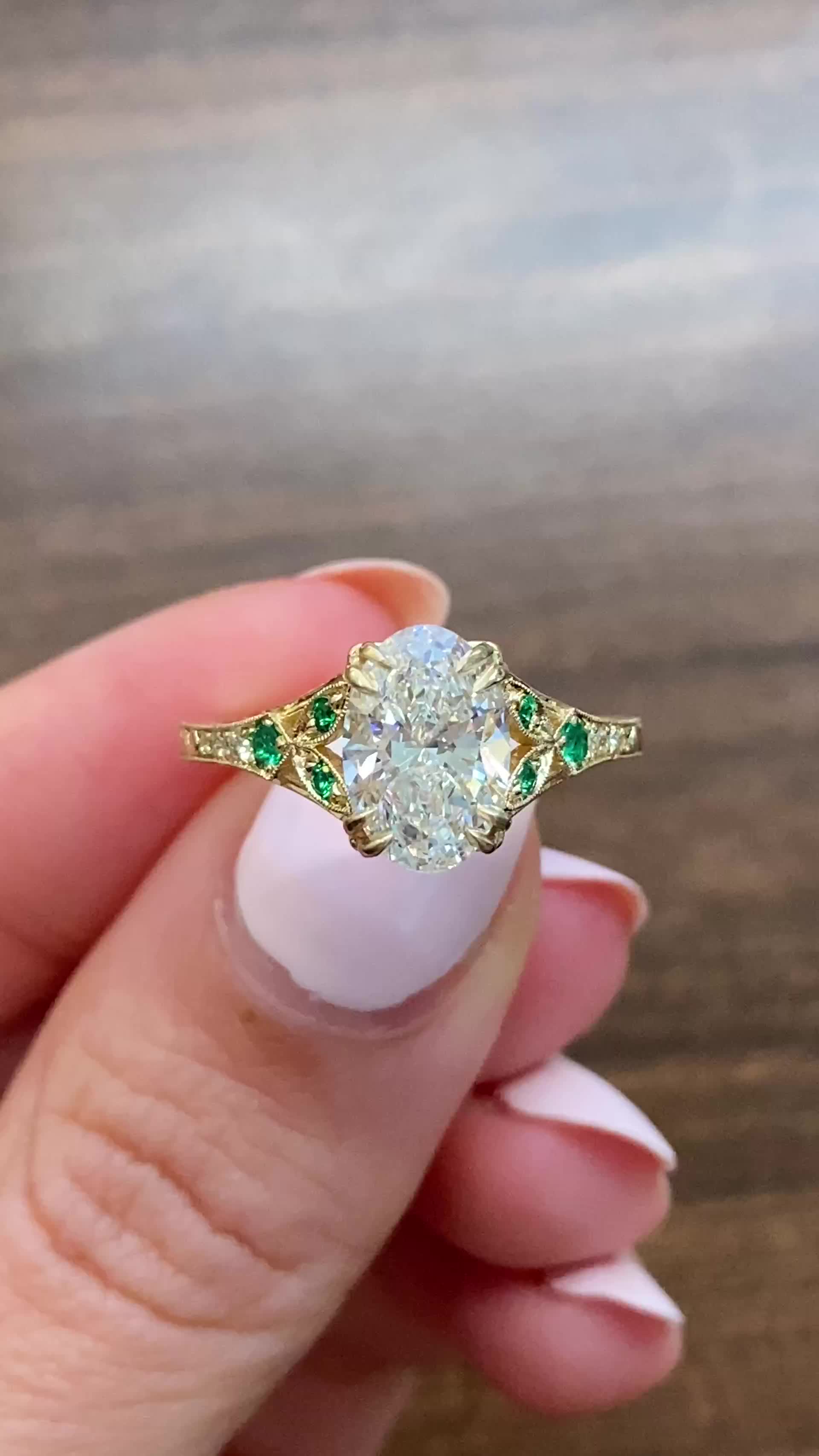 This may contain: a woman's hand holding an old diamond and emerald engagement ring on her finger