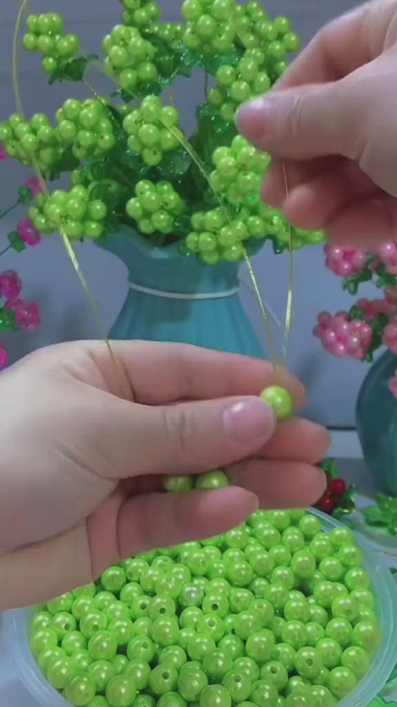 This may contain: two hands holding green beads in front of a blue vase filled with flowers