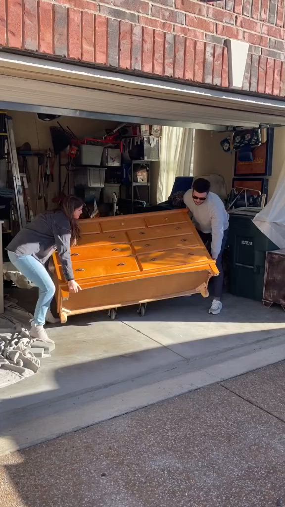 This may contain: two people looking at an old dresser in a garage with the door open to show it's contents