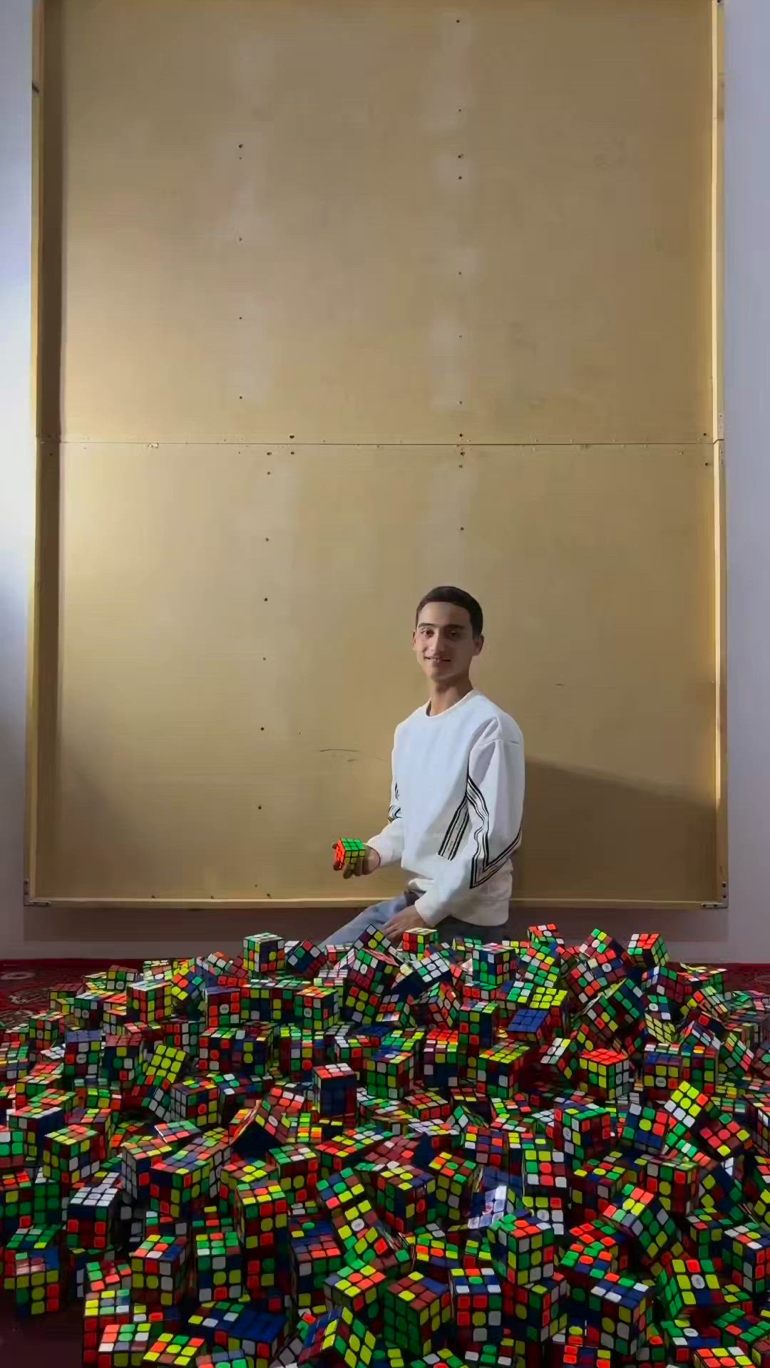 This may contain: a man standing in front of a pile of rubix cubes on the floor