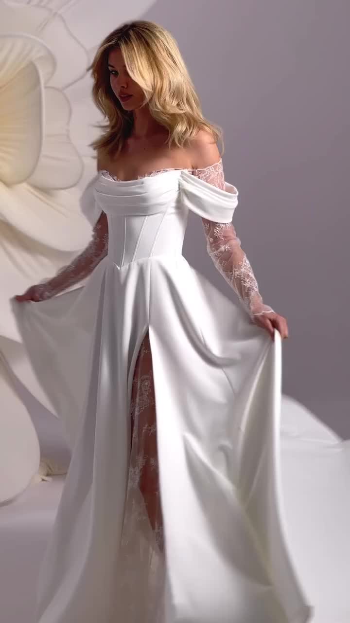 This may contain: a woman in a white wedding gown with long sleeves and an open slited skirt