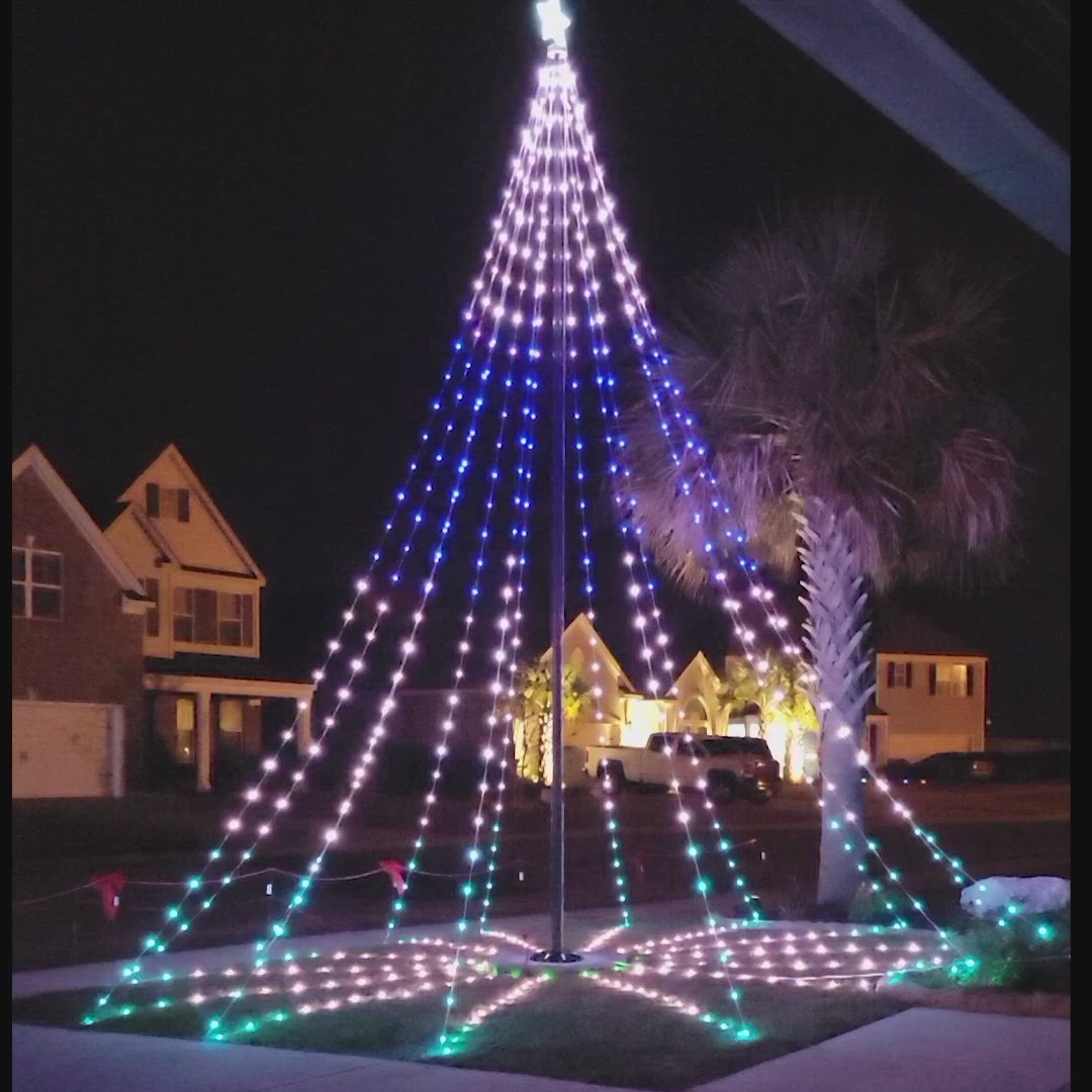 This may contain: a lighted christmas tree in the middle of a street with palm trees and houses behind it