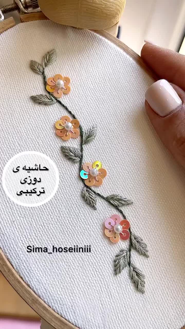 This may contain: a hand holding a cross stitched floral design on a white background with the words sima - inseini written in arabic