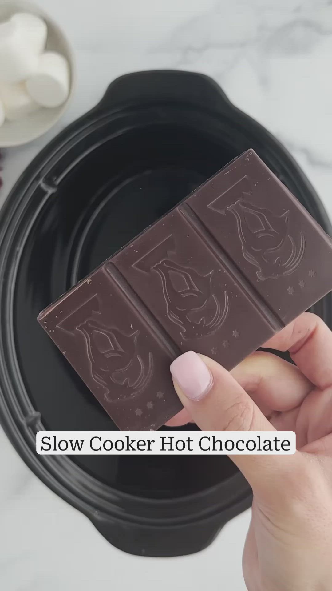 This may contain: a black bowl filled with chocolate and marshmallows on top of a white counter