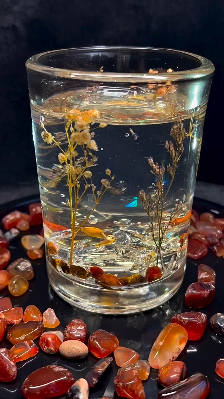 This may contain: a glass filled with water and rocks on top of a black table covered in stones