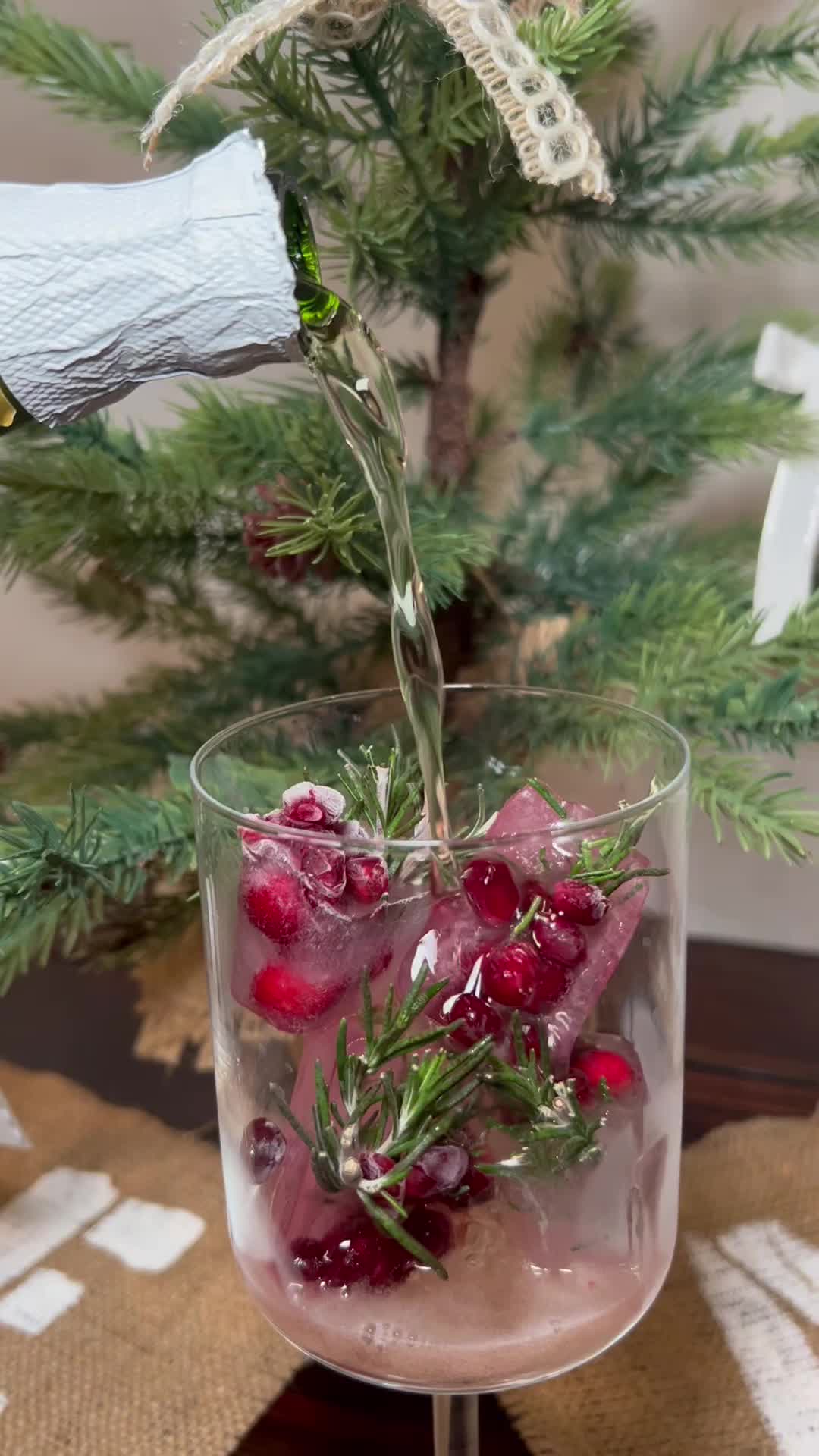 This may contain: a glass filled with ice and cranberries on top of a table next to a christmas tree