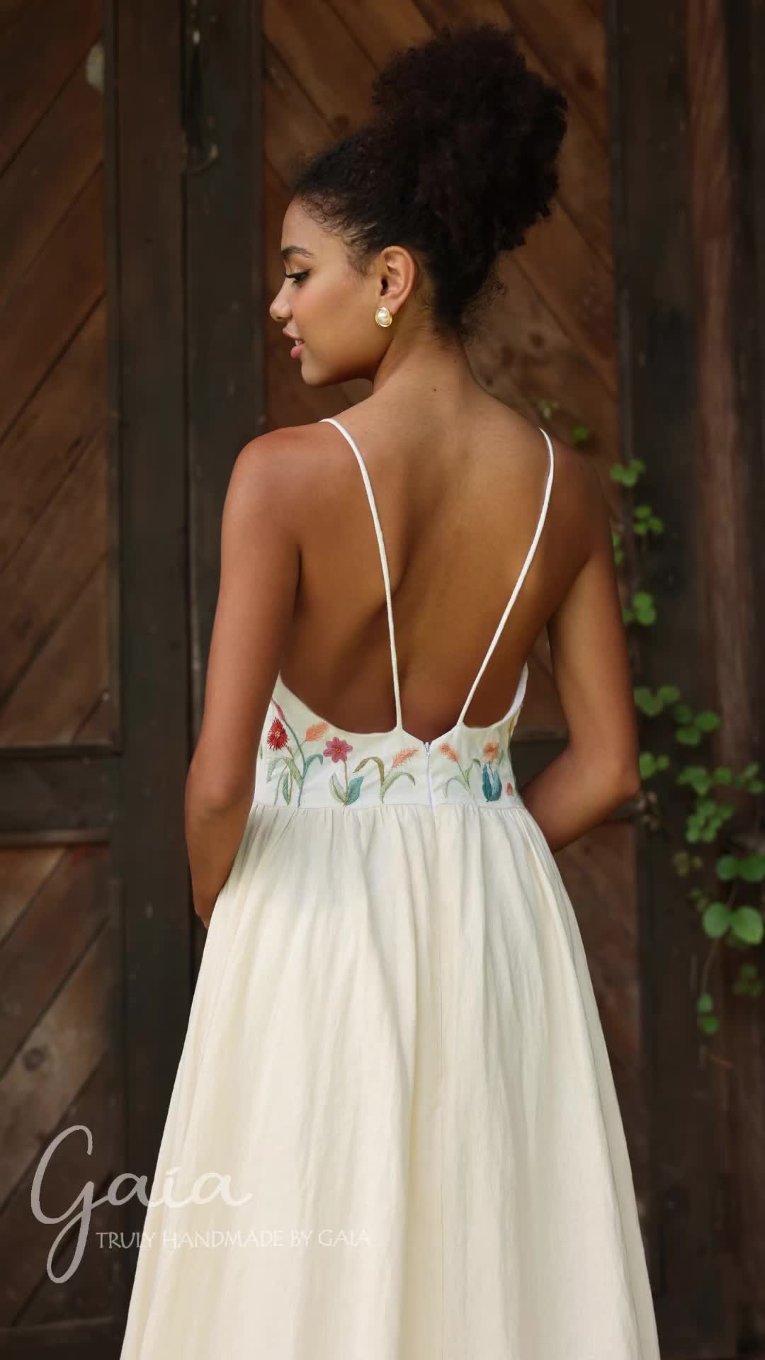 This may contain: the back of a woman wearing a white dress with floral embroidery on it, standing in front of a wooden wall