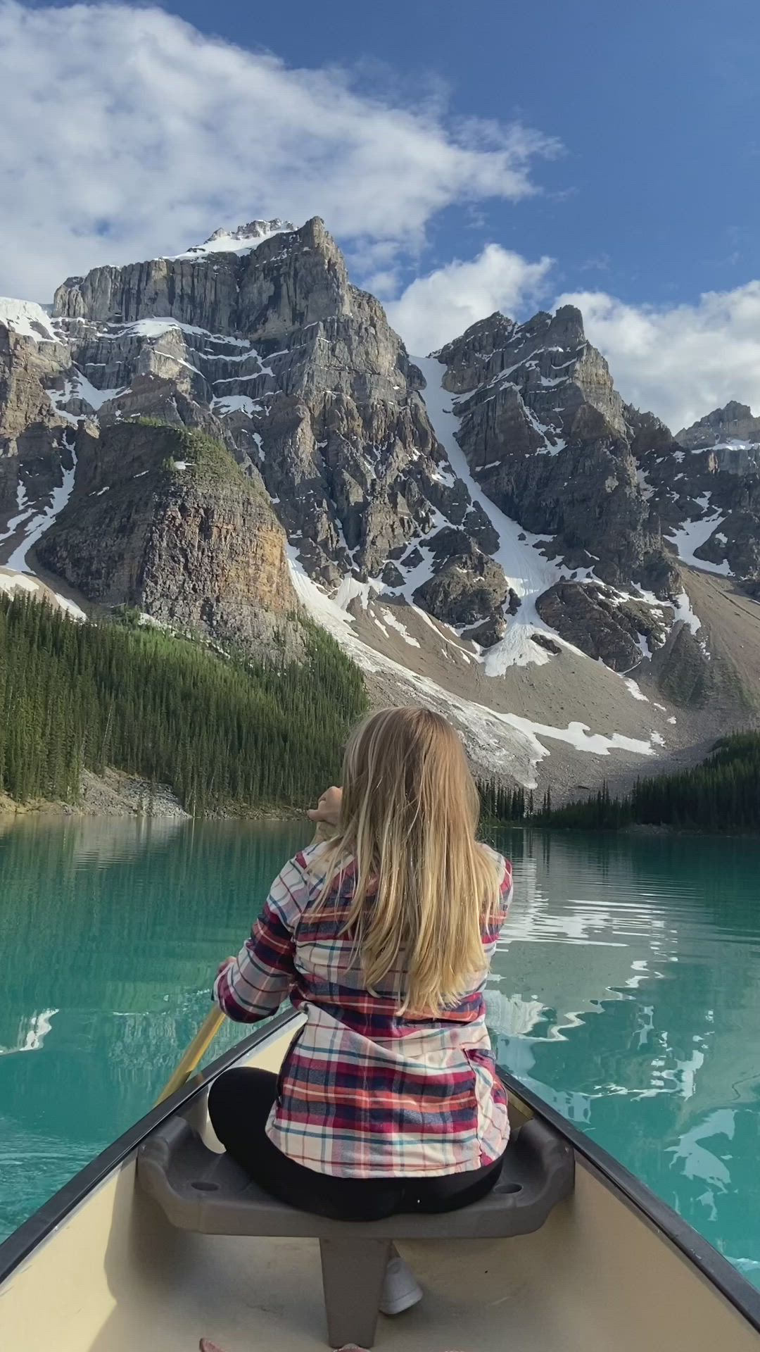 This may contain: a woman sitting in a boat on top of a lake next to snow covered mountains