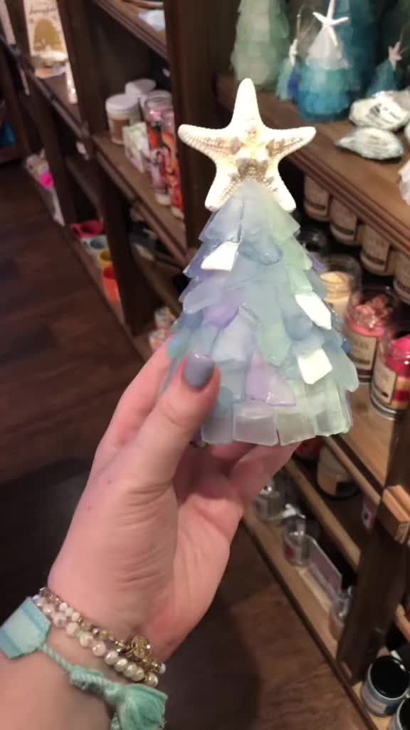 This may contain: a hand holding a paper christmas tree in front of shelves with other crafting supplies