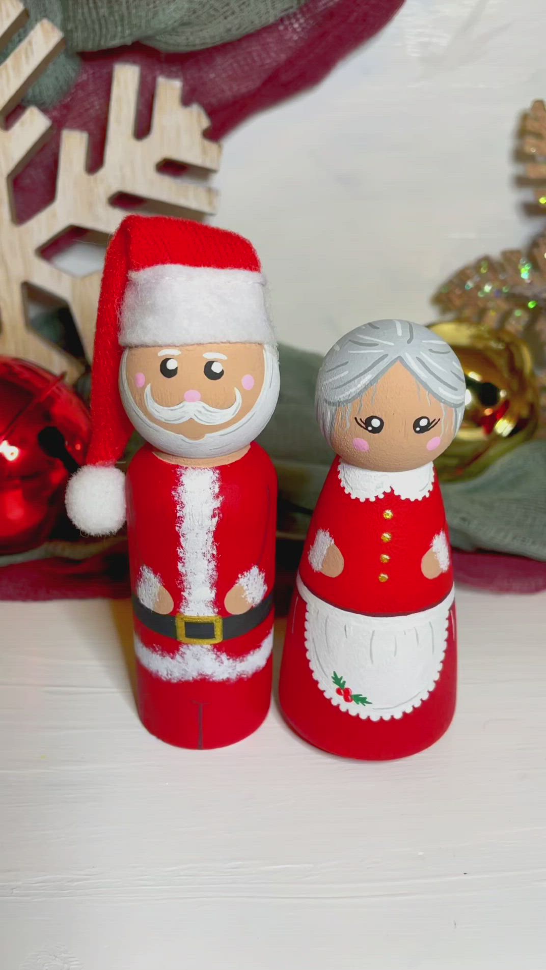 This may contain: two wooden santa and mrs claus figurines sitting on a table next to christmas decorations