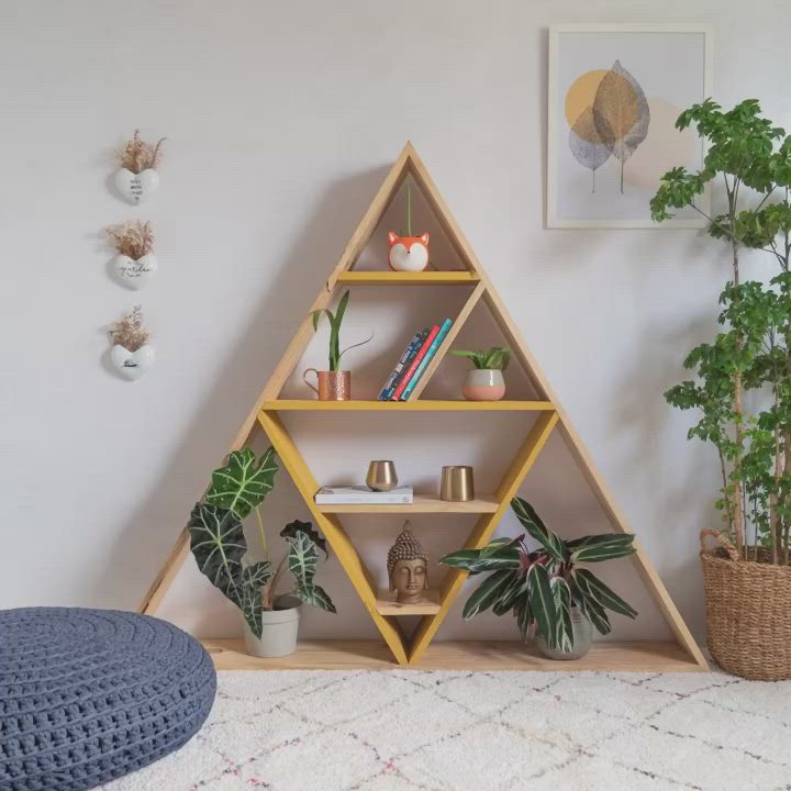 This may contain: a triangle shaped shelf with potted plants and books on it next to a rug