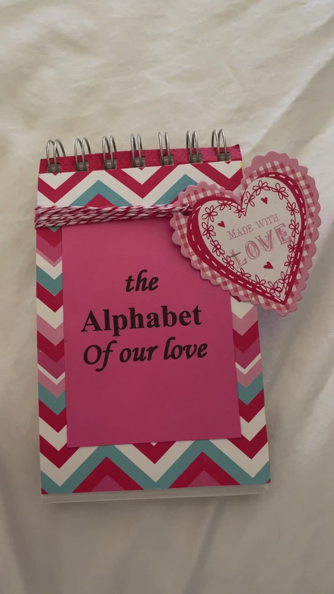 This may contain: a hand holding a pink notebook with the alphabet of our love written on it and a heart