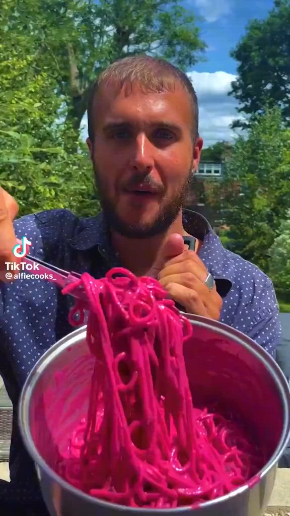 This may contain: a man holding a large metal bowl filled with pink noodles