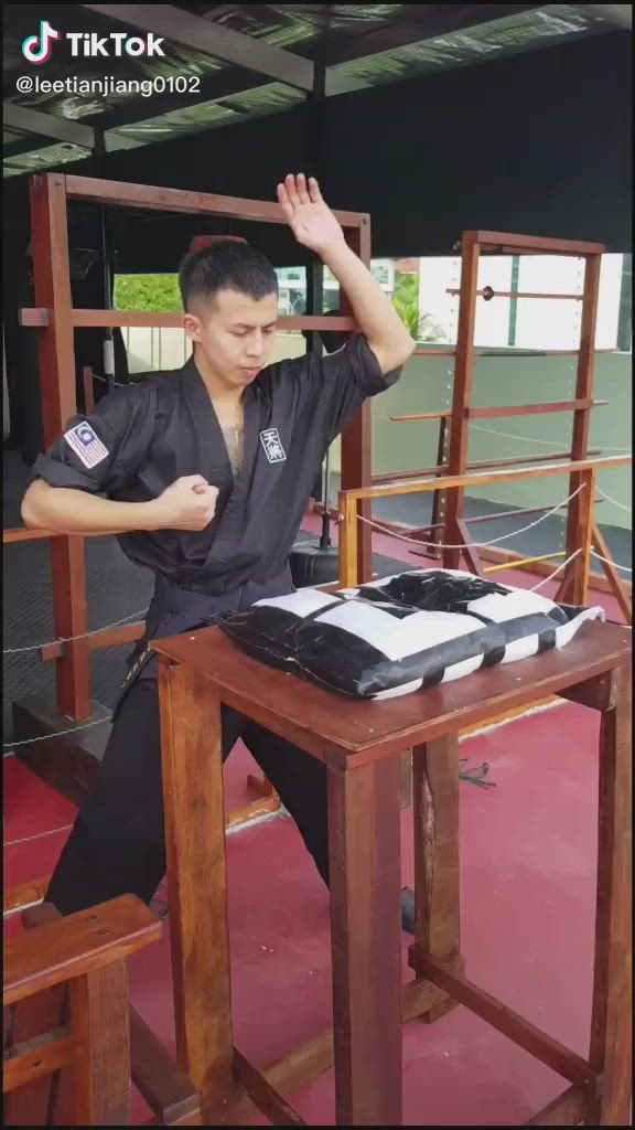 This may contain: a man sitting at a desk with his hand up in the air while wearing black