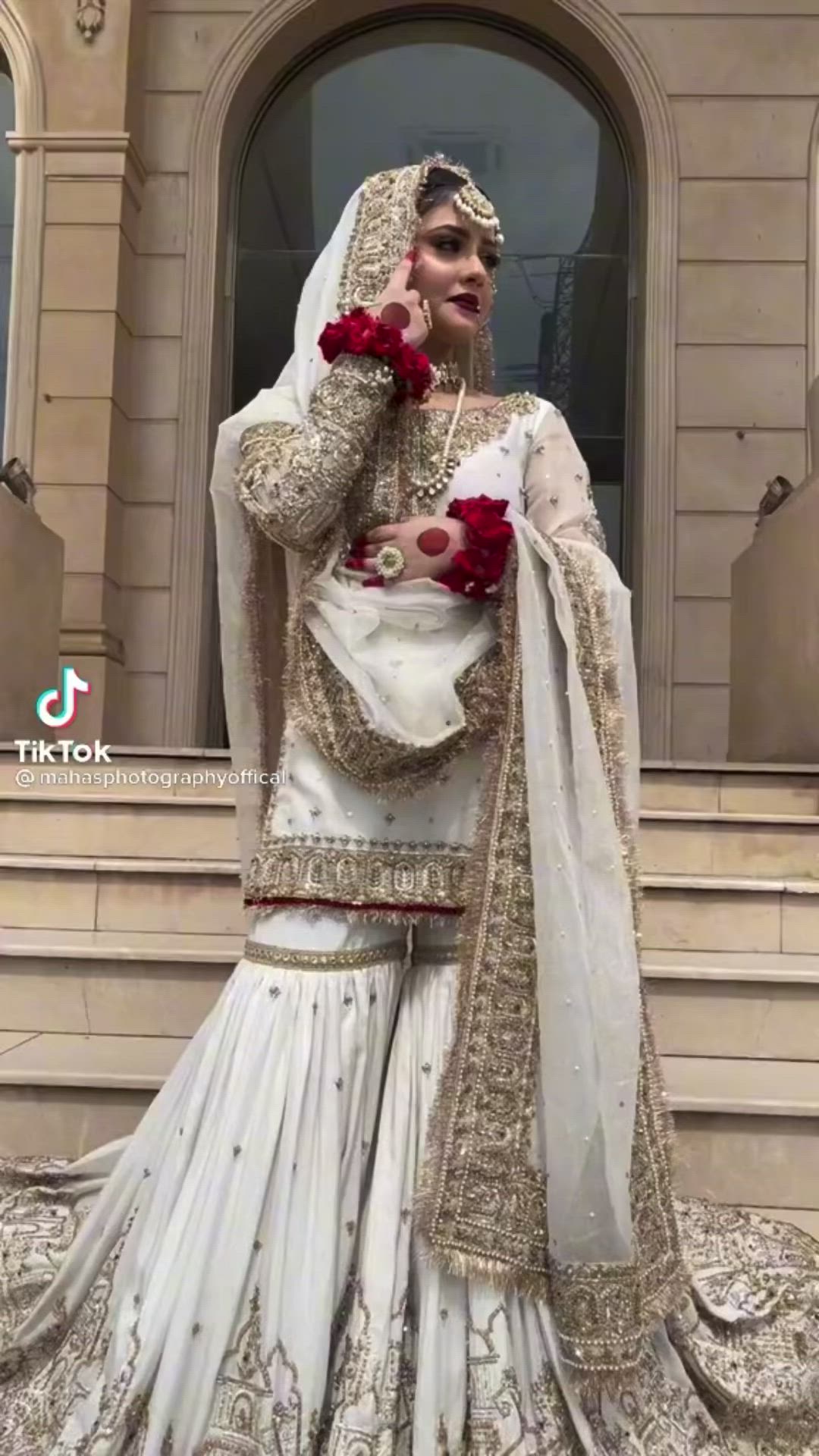 This may contain: a woman in a white and red bridal outfit is standing on steps with her hands to her face