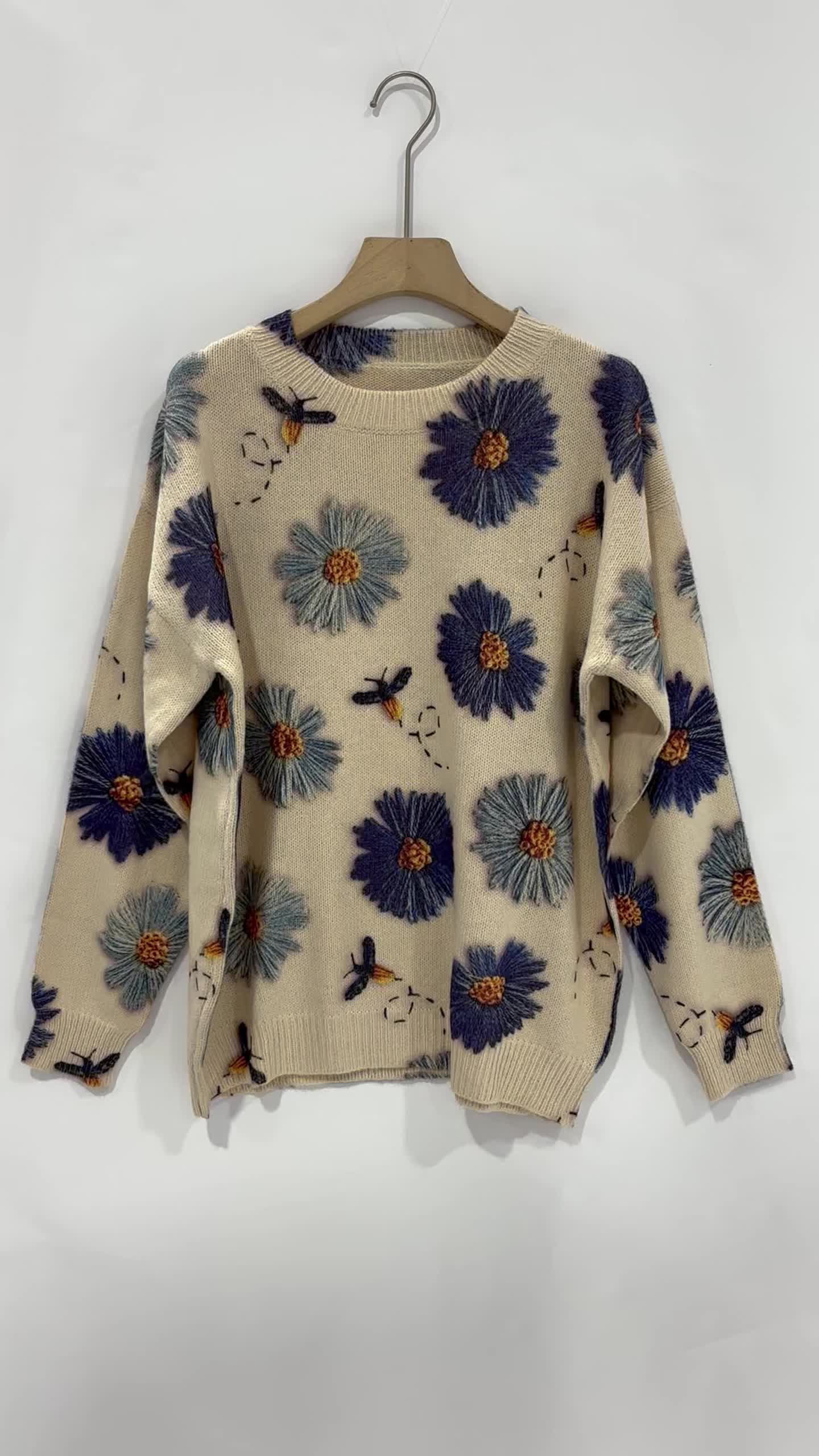 This may contain: a sweater with blue flowers on it hanging from a clothes hanger in front of a white wall