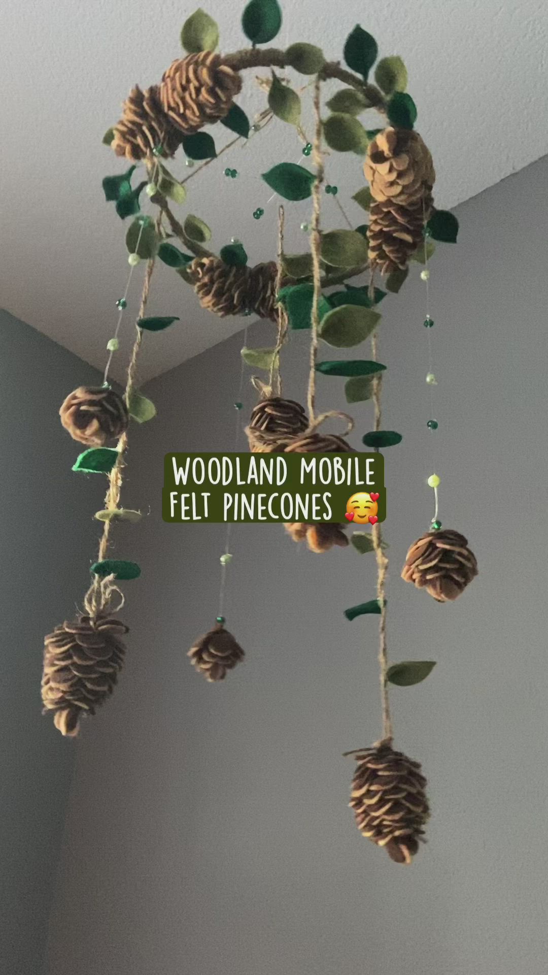 This may contain: a mobile made out of pinecones hanging from the ceiling with words woodland mobile