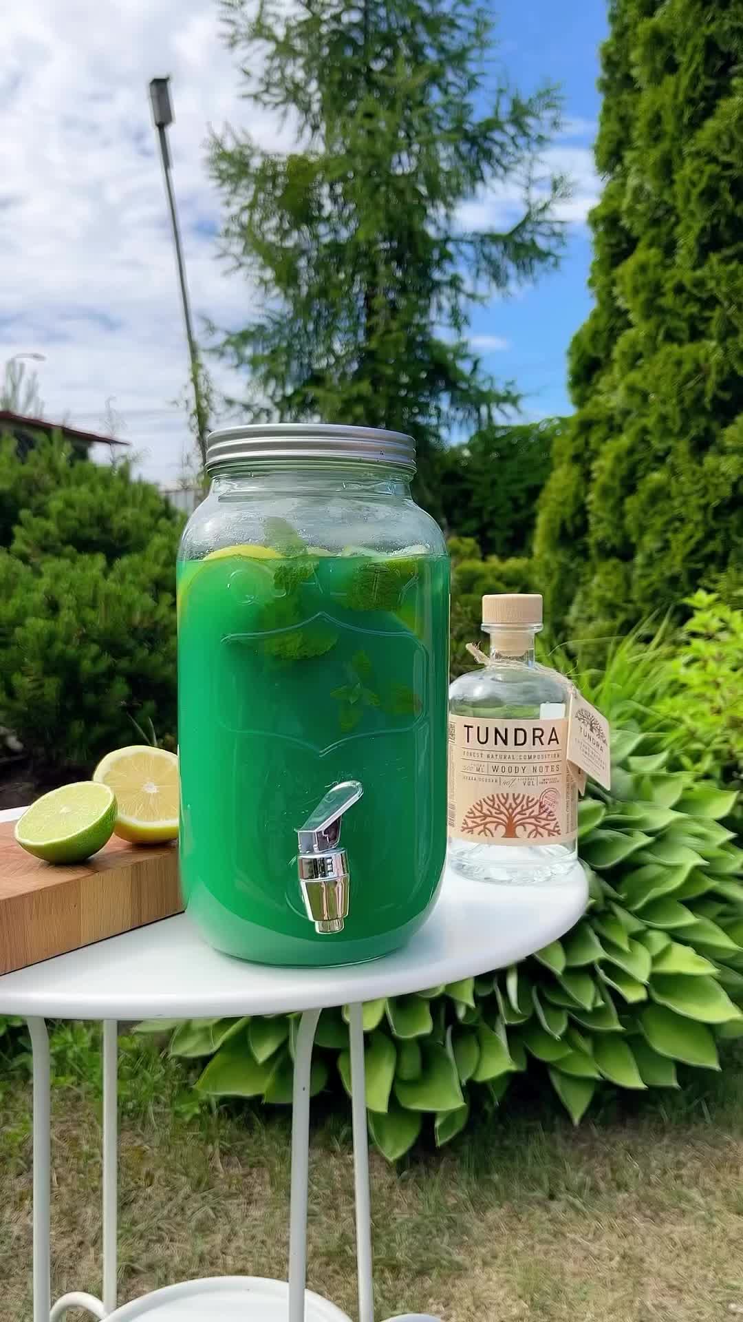 This may contain: there is a large jar with green liquid on it next to some lemons and limes