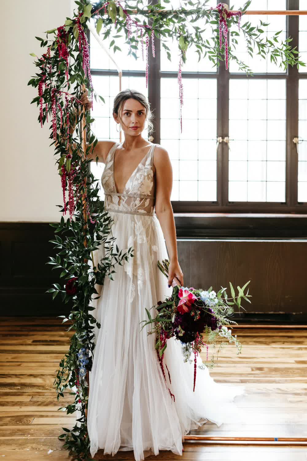 This may contain: a woman standing in front of a wedding arch with flowers and greenery on it