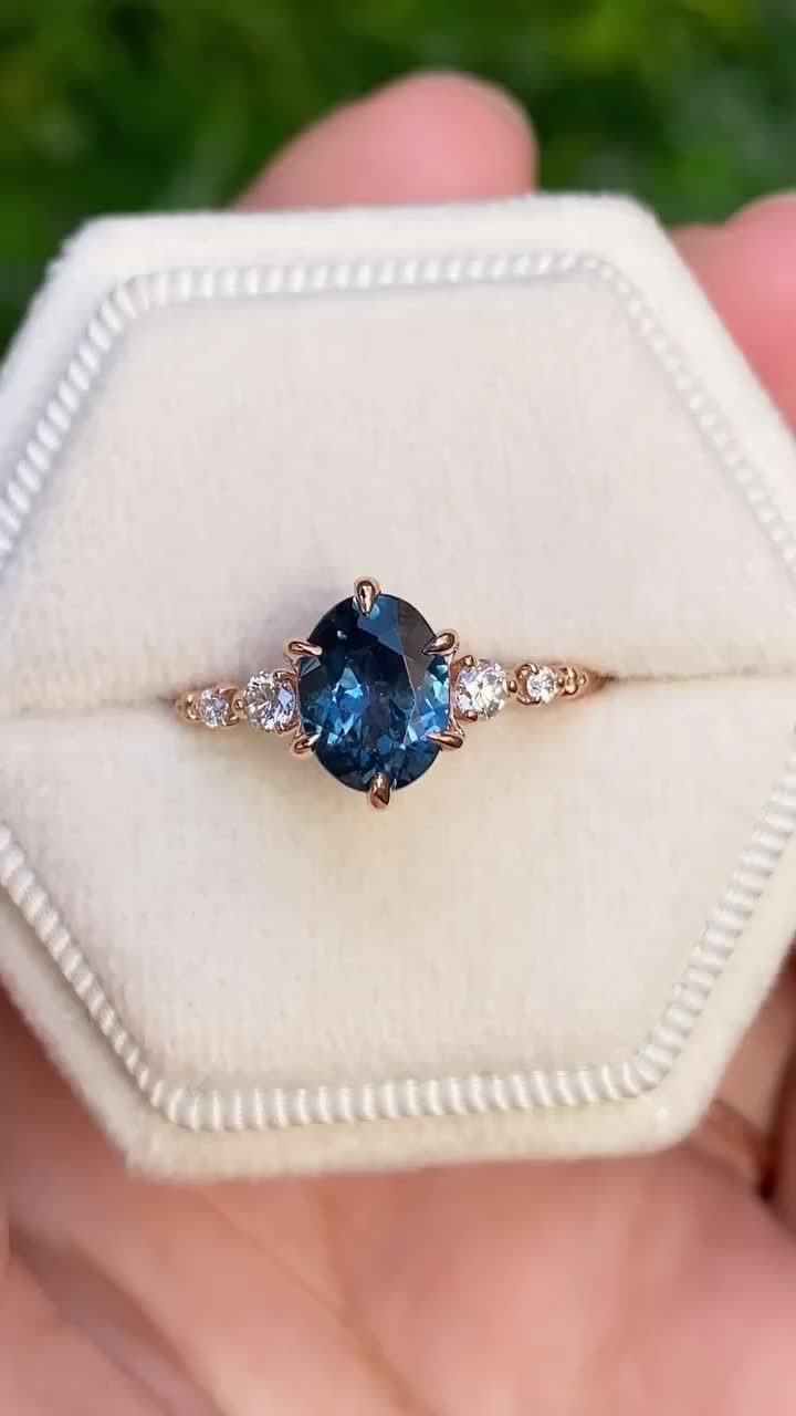 This may contain: a person holding a ring with a blue stone in it's center and two diamonds on the side