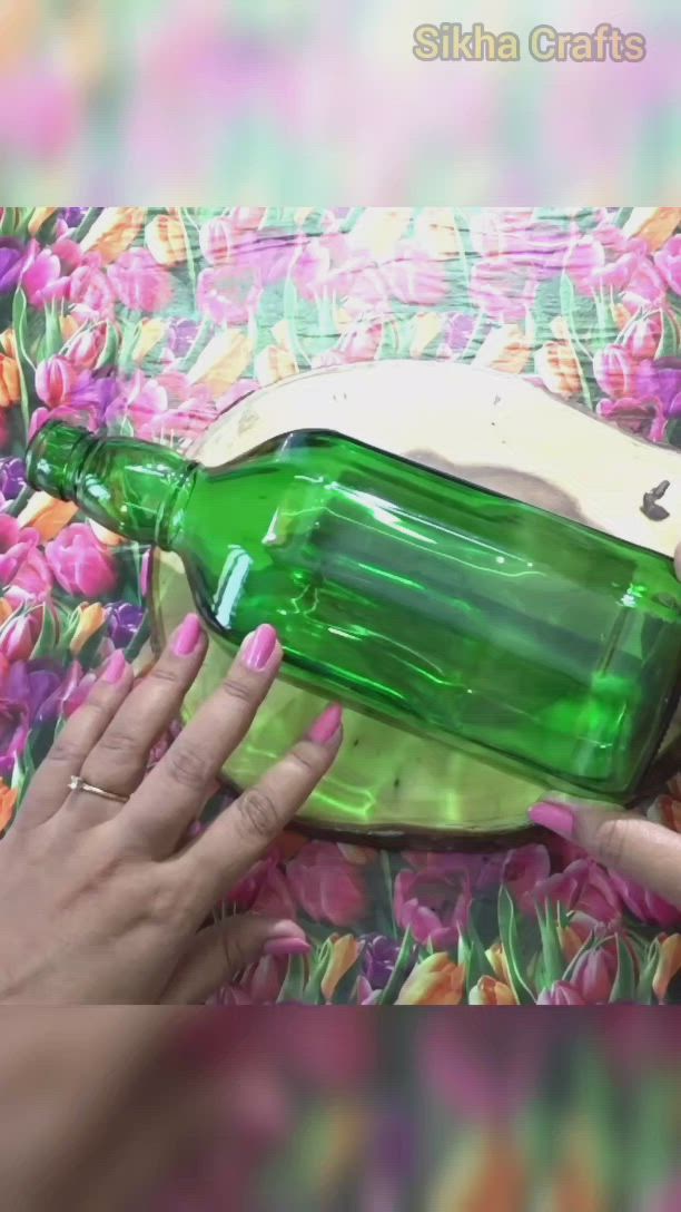 This may contain: a person holding a green glass bottle with a wooden handle on top of it and pink flowers in the background