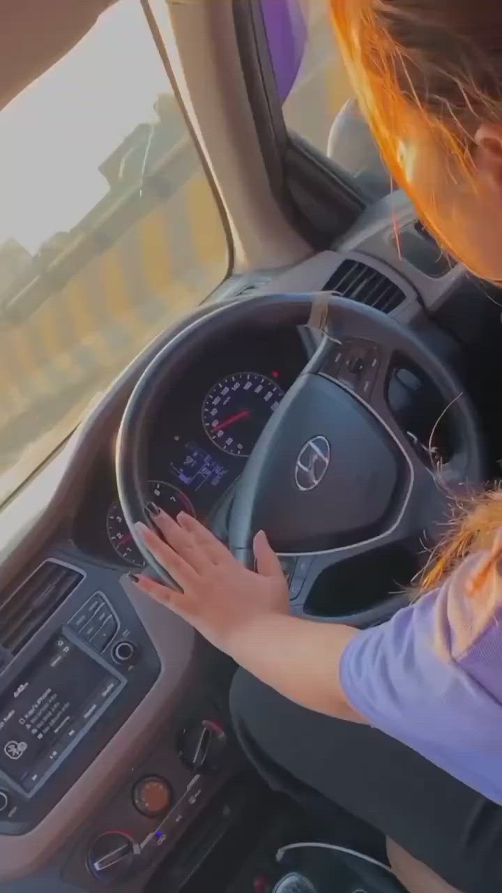 This may contain: a woman driving a car with her hands on the steering wheel while wearing a purple shirt