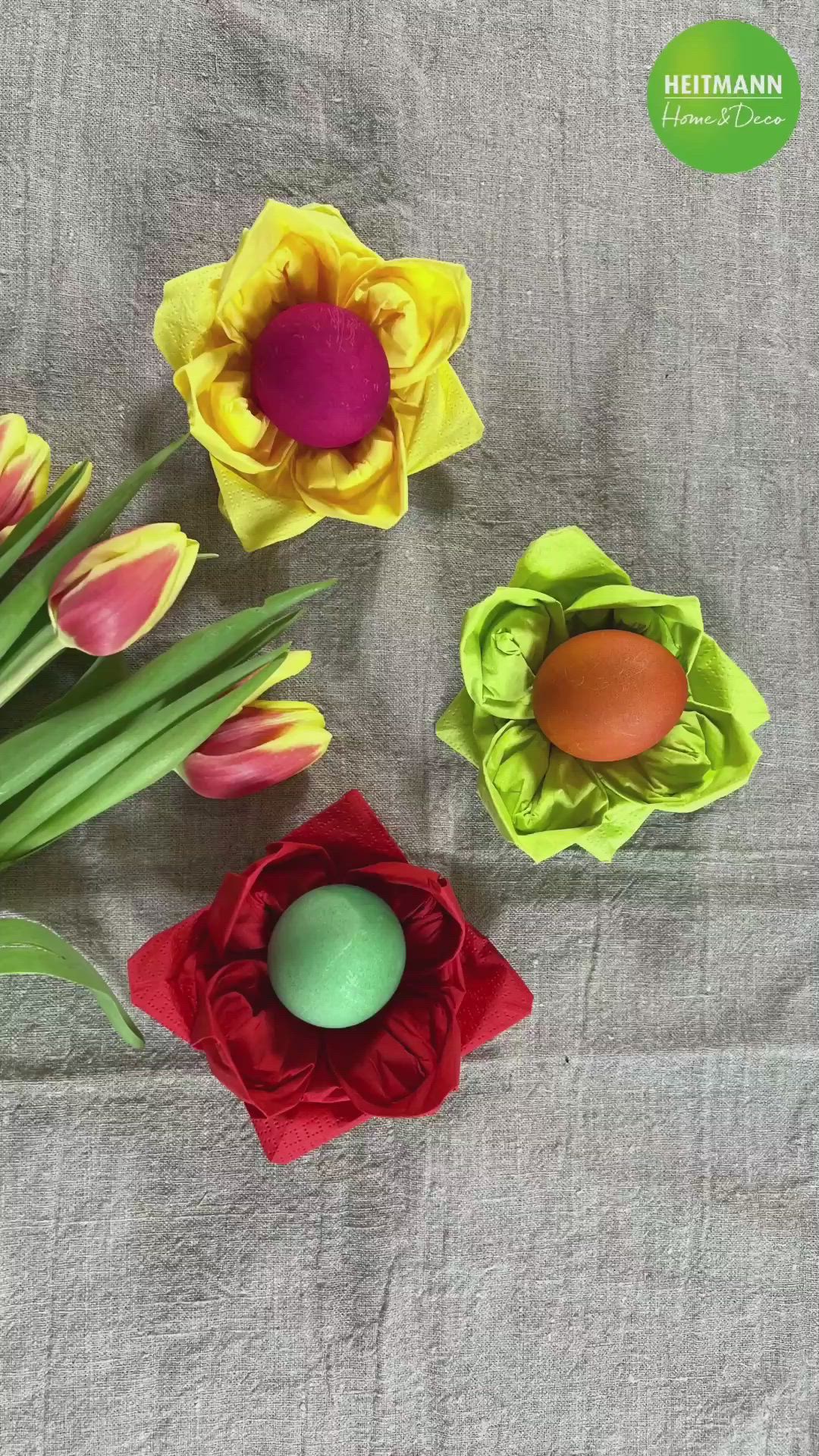 This may contain: three paper flowers and an egg are on a gray tablecloth with a green sticker