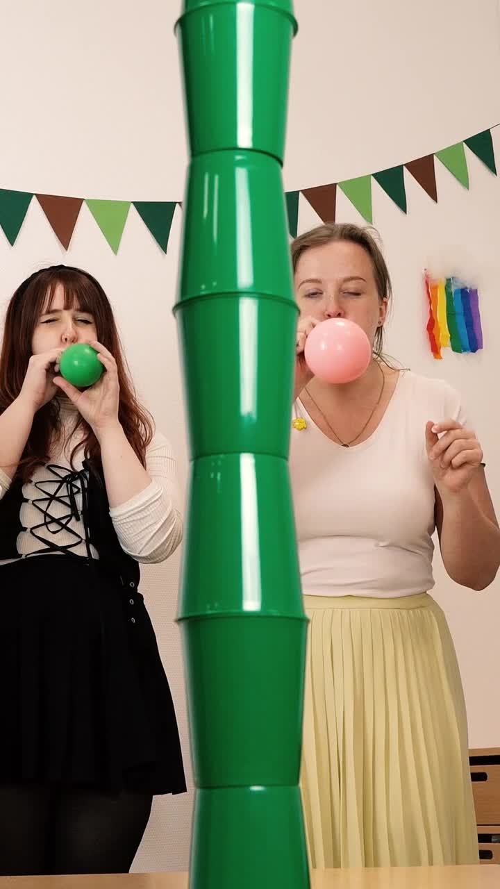 This may contain: two women standing next to each other near a large green vase with pink balls in it