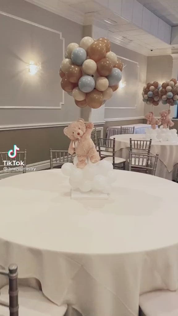 This may contain: a teddy bear sitting on top of a table with balloons in the shape of animals