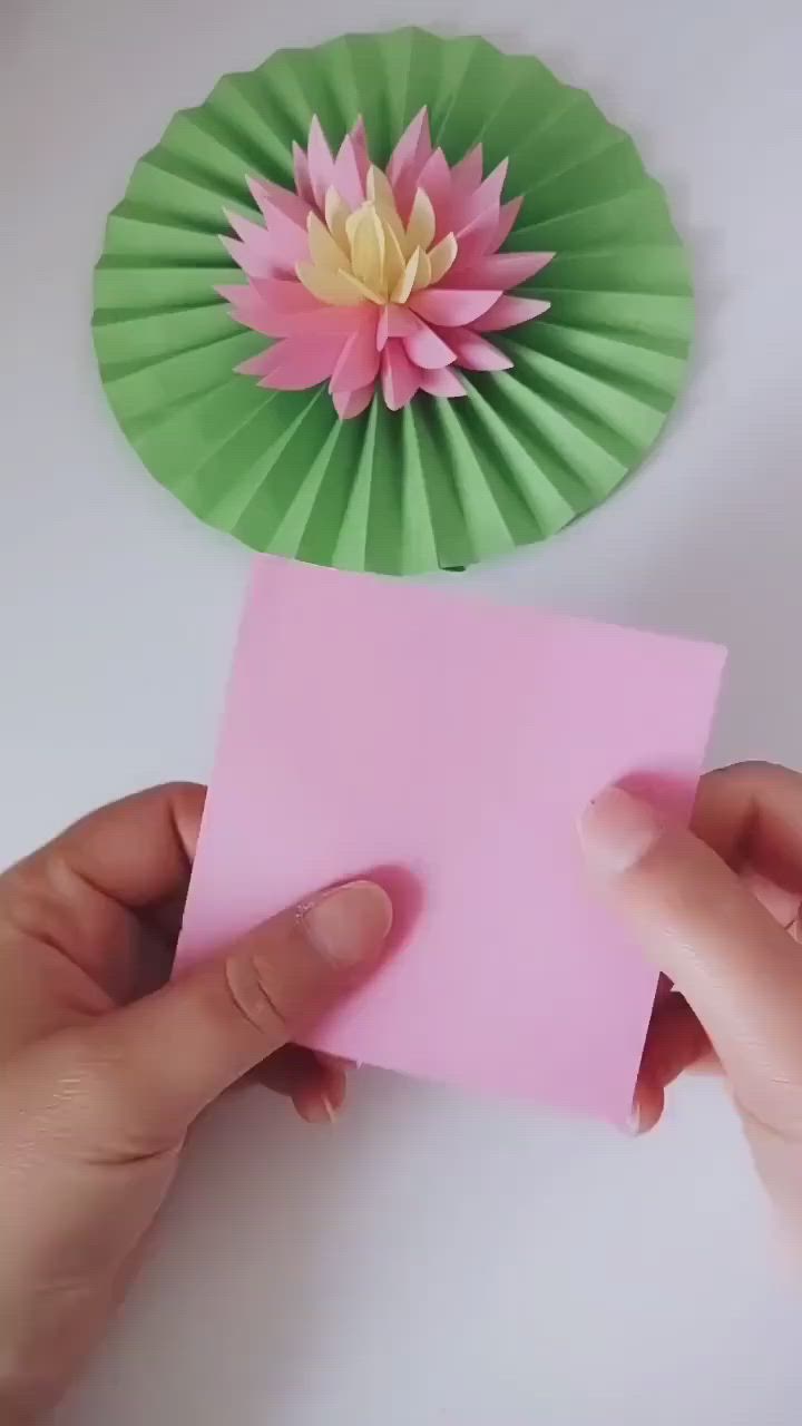 This may contain: someone is holding a piece of pink paper with a flower on it and a green fan behind them