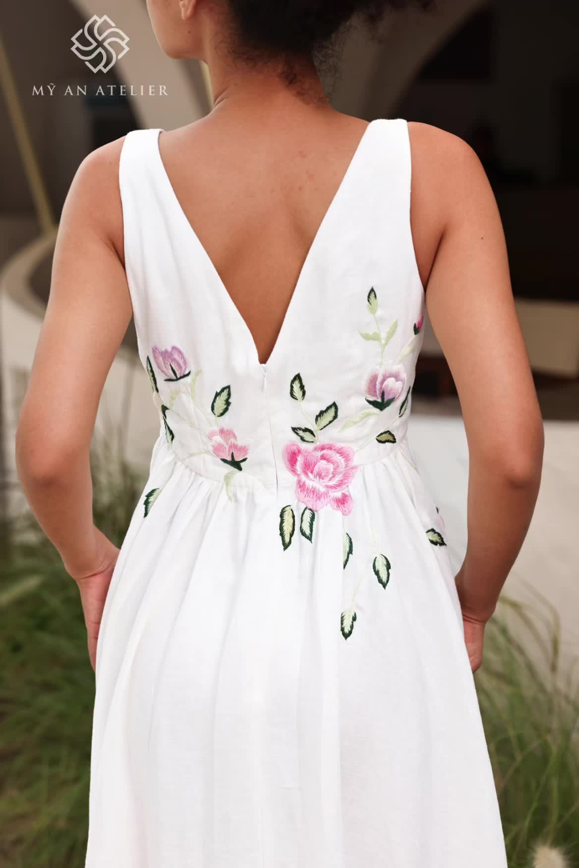 This may contain: the back of a woman's white dress with pink flowers and leaves on it