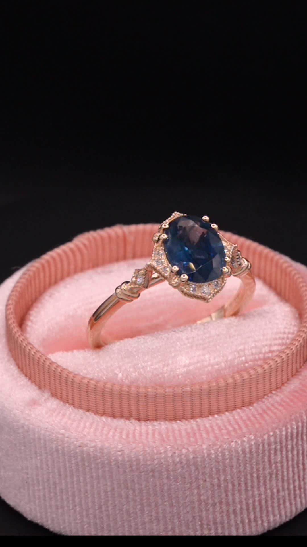 This may contain: a ring with a blue stone in it on a pink velvet band next to a black background