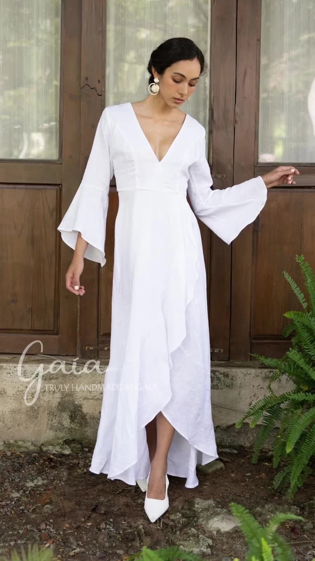 This may contain: a woman standing in front of a wooden door wearing a white dress with bell sleeves