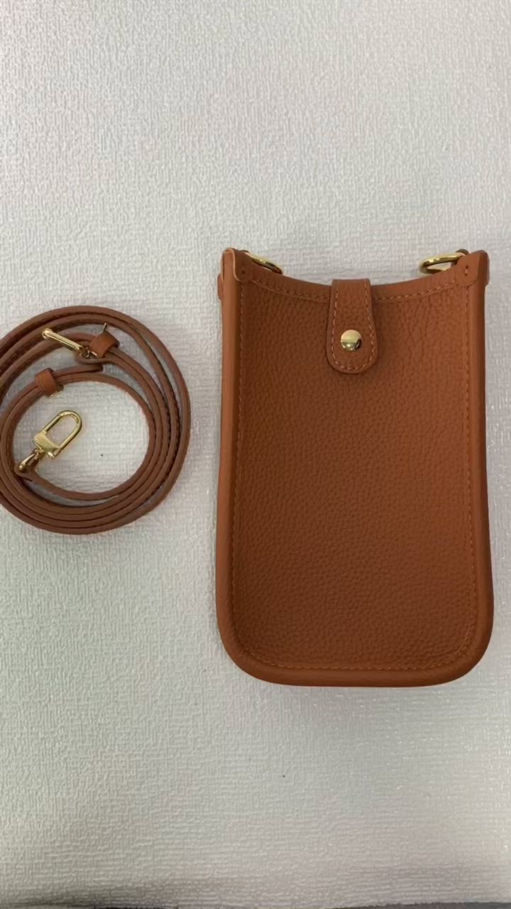 This may contain: a brown purse sitting on top of a white wall next to a leather cord and phone holder