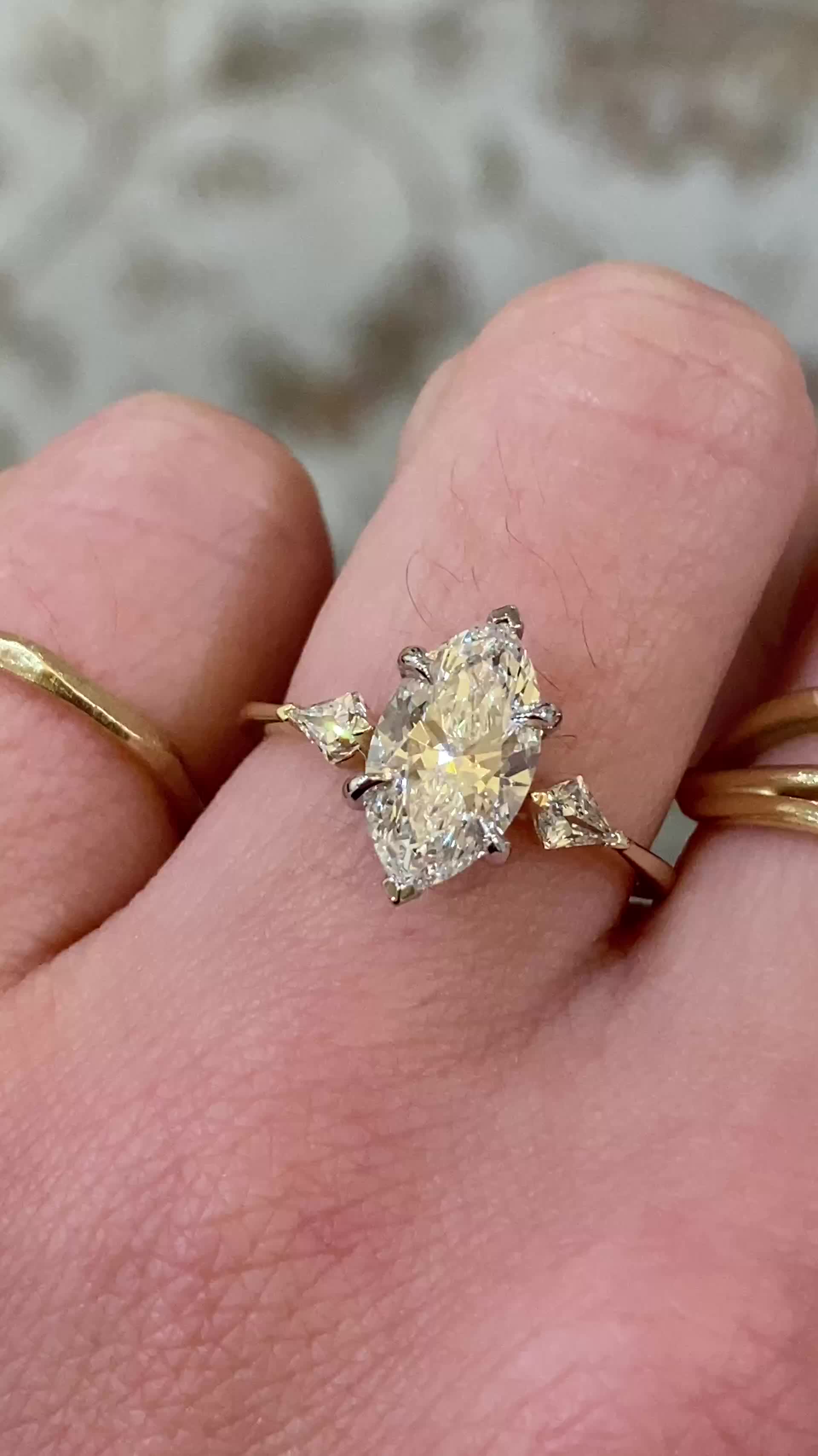 This may contain: a woman's hand with two gold rings and an engagement ring on top of her finger