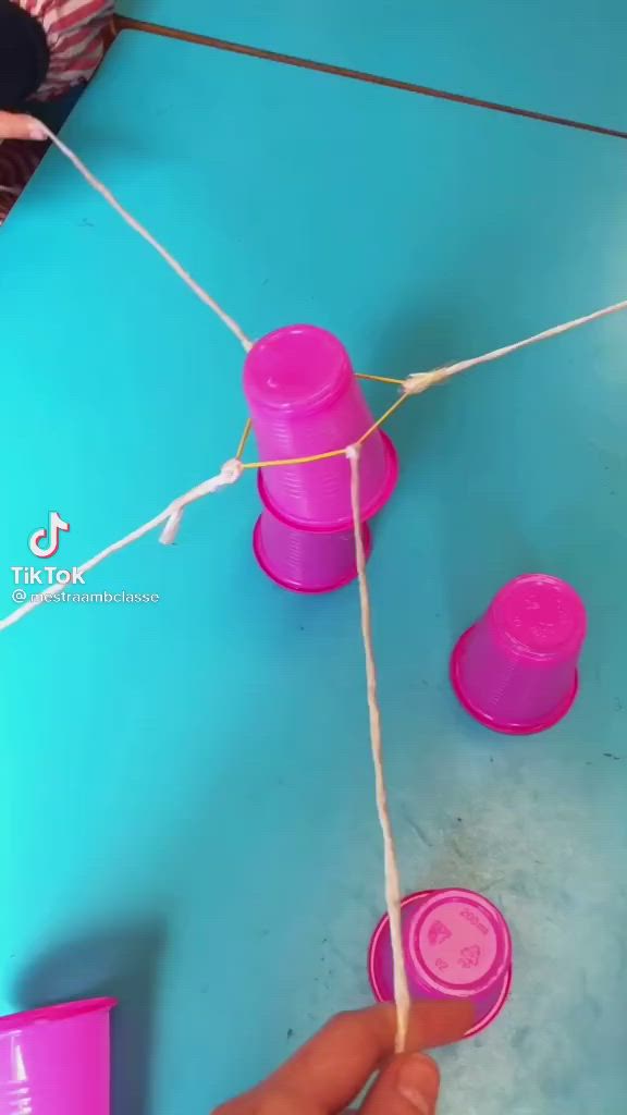 This may contain: someone is stringing together pink cups on a blue table