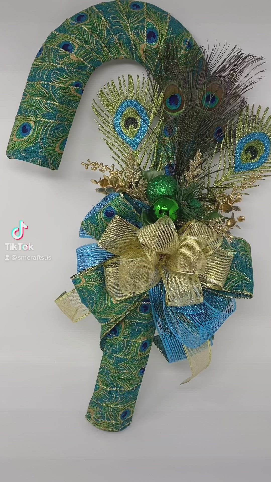 This may contain: a peacock themed wreath with gold and blue ribbons, feathers, and green bow on a white background