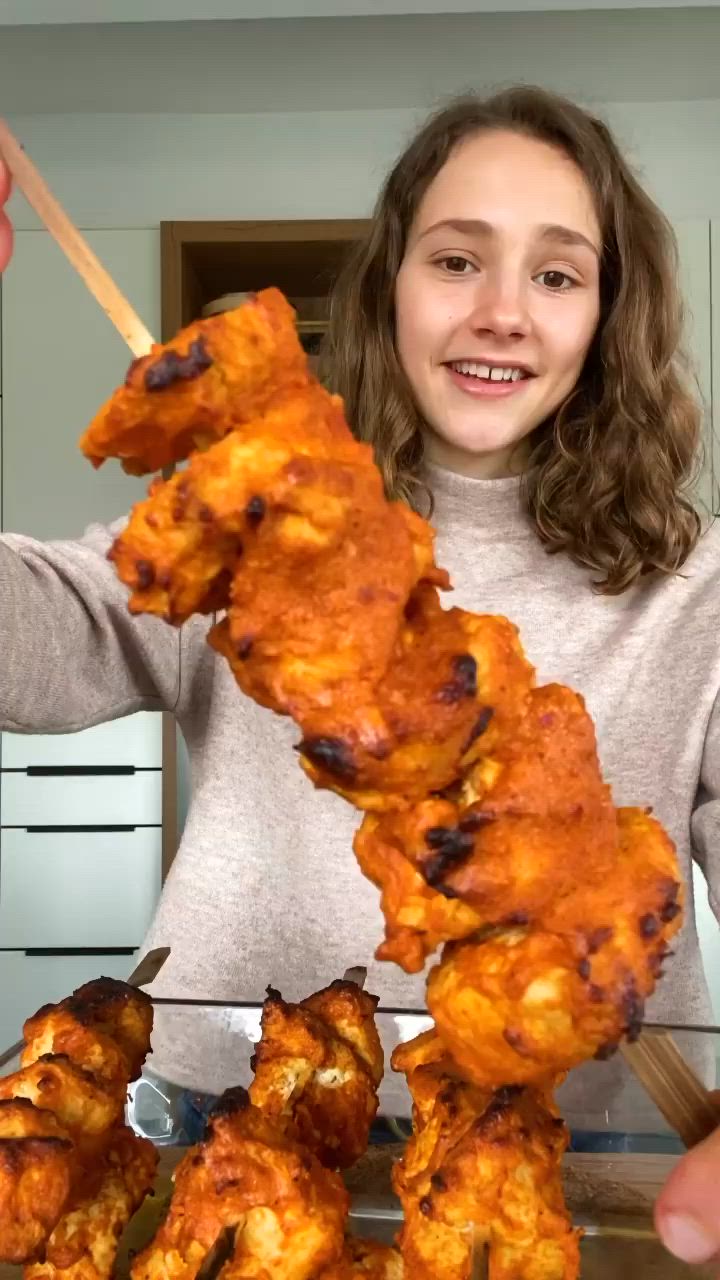 This may contain: a girl is holding up some chicken skewers