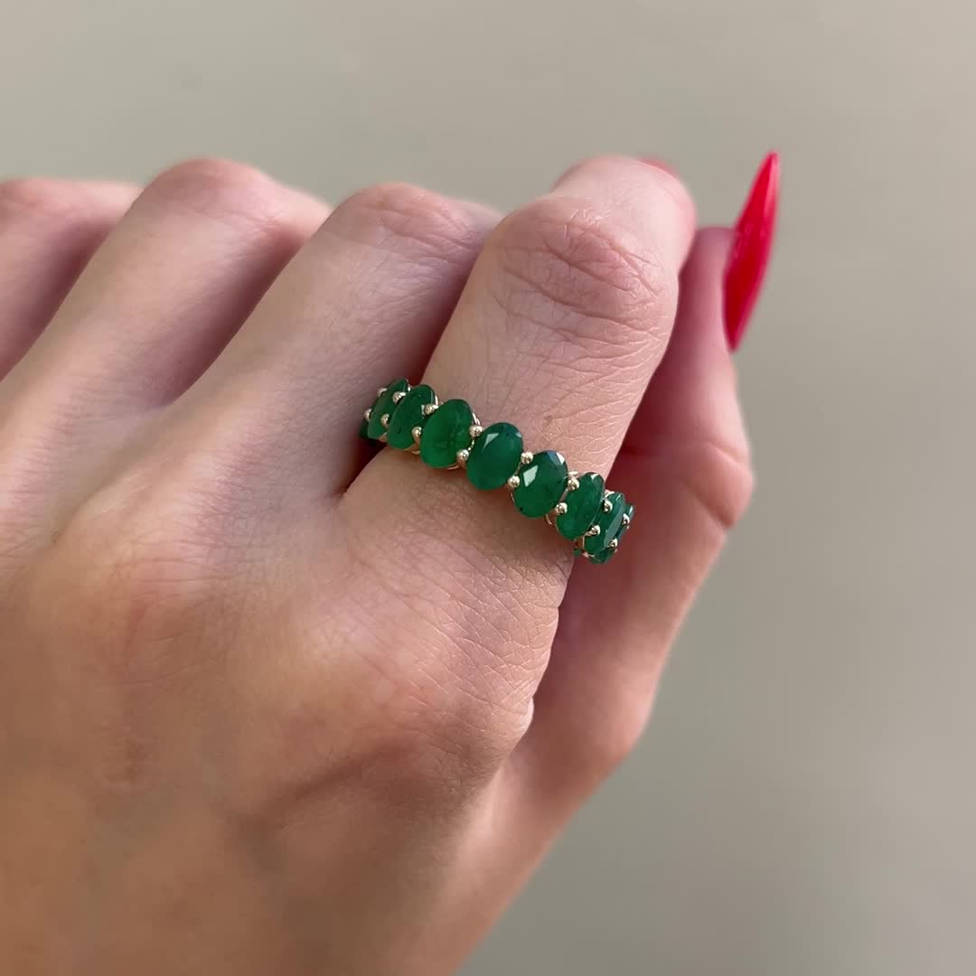 This may contain: a woman's hand holding a ring with three green stones on it and a red nail