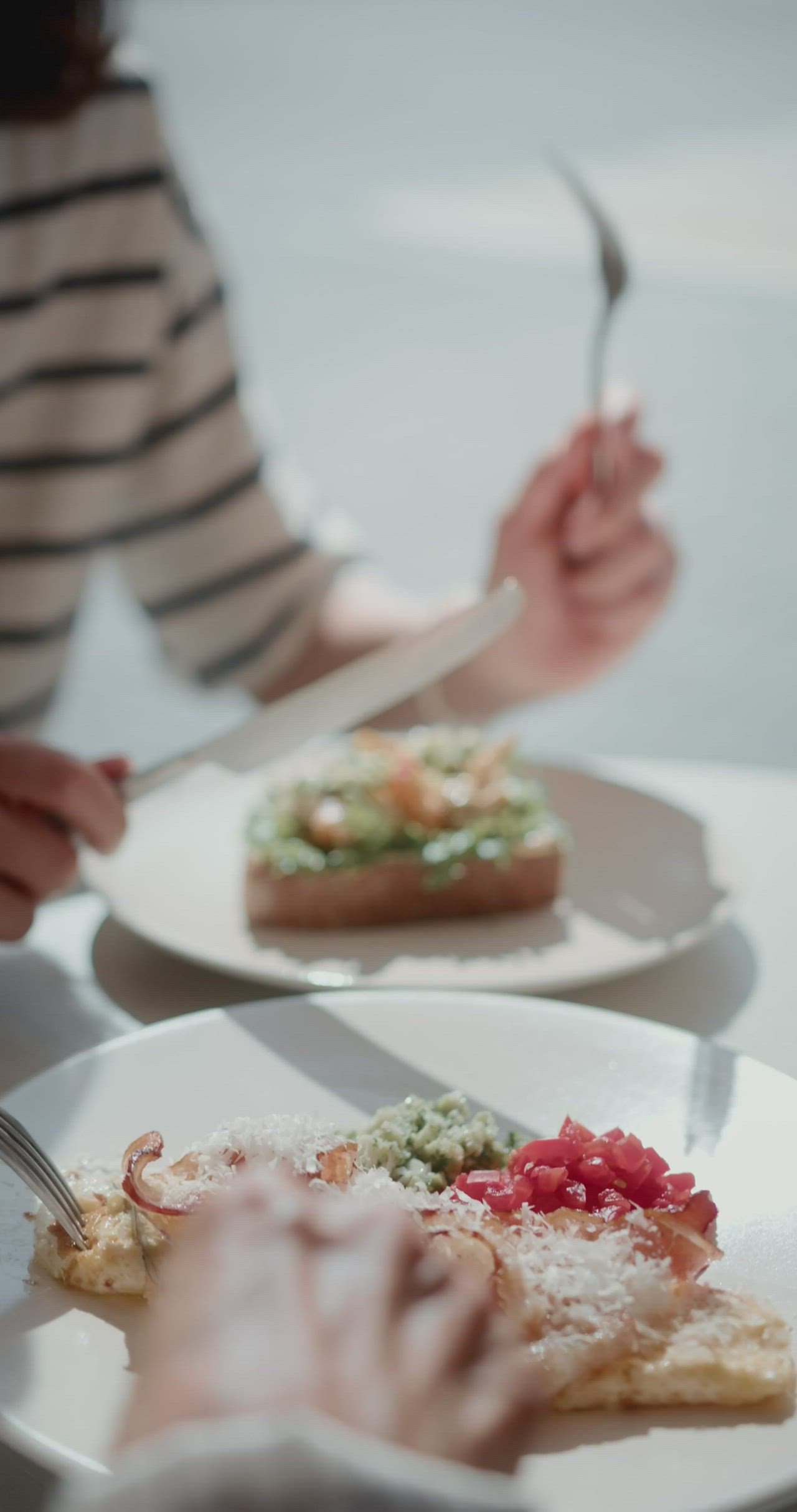 This may contain: two white plates with food on them, one being eaten by someone holding a fork and knife