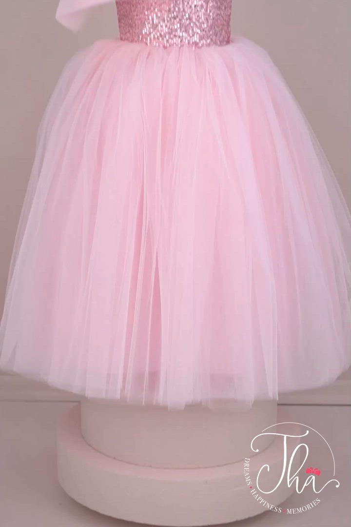 This contains: A pink sleeveless bridesmaid wedding dress that has a pink sequin top and a full pink skirt which has layers of pink tulle. It is decorated with a tulle bow on right shoulder.