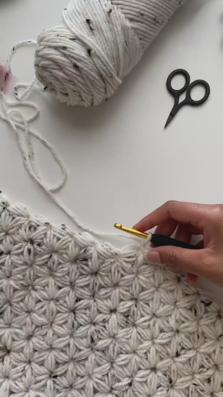 This may contain: two hands crocheting together on a table with yarn, scissors and twine