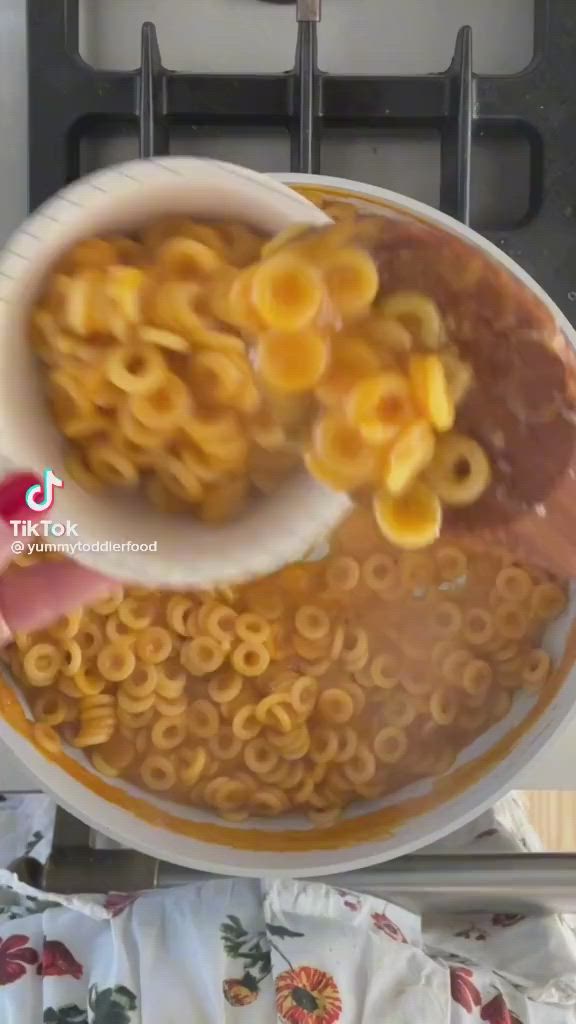 This may contain: a bowl of macaroni and cheese being stirred with a spoon in front of an oven